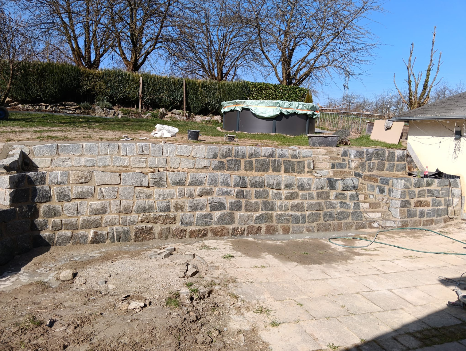 Gemauerte Natursteinmauer in einem Hanggrundstück mit Pool dahinter