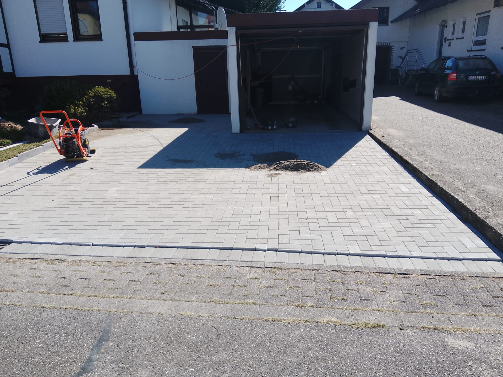 Frisch gepflasterte Einfahrt mit Rüttelplatte vor einer Garage
